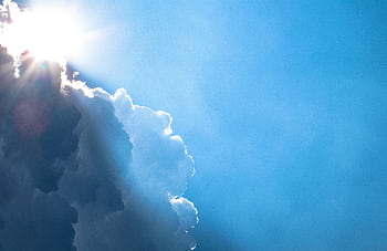 Bright sunlight streams through dramatic clouds in a vivid blue sky. HD wallpaper
