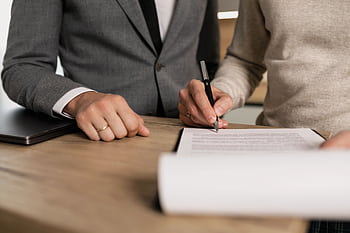 Close-up of businessmen signing documents at a wooden table in an office. HD wallpaper