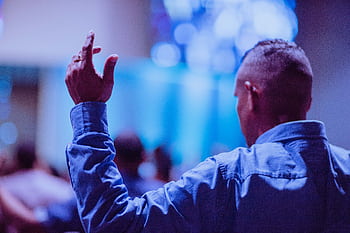 Back view of a man raising hand in prayer at a church service indoors. HD wallpaper