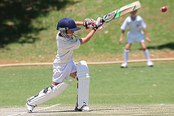 Young cricketer in white gear executing a sweep shot on a sunny day. HD wallpaper