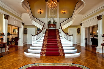 Grand staircase with red carpet in a luxurious hotel lobby, highlighted by a chandelier. HD wallpaper