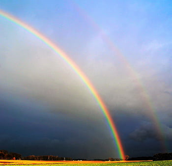 Double rainbow arching over a serene rural field against a dramatic sky. HD wallpaper