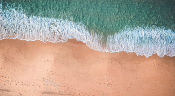 Aerial view of gentle waves meeting sandy beach on a sunny day, perfect for relaxation. HD wallpaper