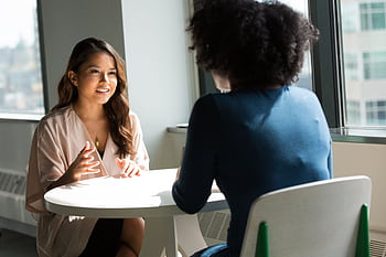 Two women sitting at a table having a professional discussion in a bright office setting. HD wallpaper