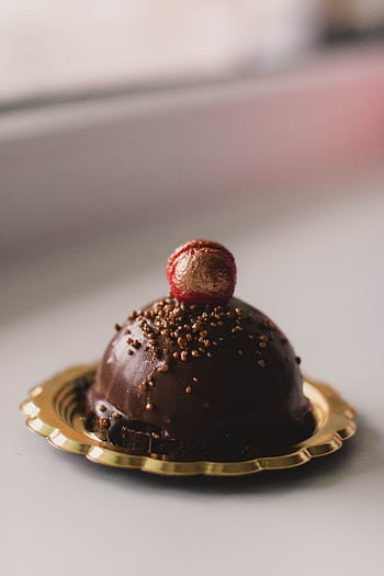 Luxurious chocolate dessert on gold plate with red candy topping, perfect for indulgence. HD phone wallpaper
