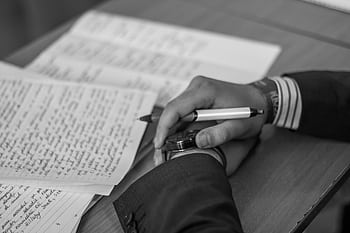 Close-up of a hand holding a pen over pages of writing on a desk. HD wallpaper