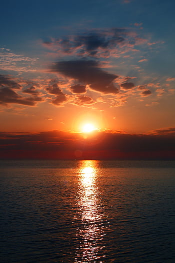 Breathtaking sunset over a calm ocean with vibrant colors and dramatic clouds. Perfect for serene backgrounds. HD phone wallpaper