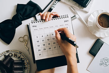 Top view of hands using a planner with coffee and accessories, focused on May 2021 calendar. HD wallpaper