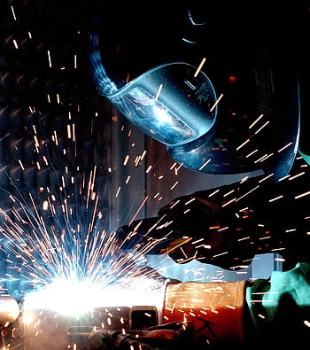 A focused welder works with metal in an industrial setting, creating vibrant sparks. HD phone wallpaper