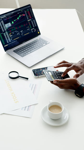 A businessman using a laptop and smart to analyze stock market trends indoors. HD phone wallpaper