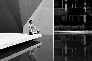 A woman meditating by a poolside, reflecting tranquility and focus in a minimalist setting. HD wallpaper