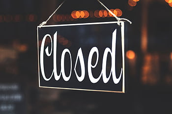 A close-up of a 'Closed' sign hanging against a blurred, bokeh background, creating a warm, inviting atmosphere. HD wallpaper
