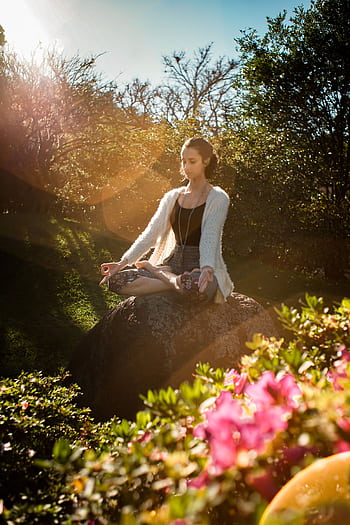 Woman in tranquil meditation pose outdoors, bathed in sunlight, surrounded by lush greenery. HD phone wallpaper