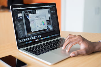 A person editing on a laptop in an office, showcasing technology use. HD wallpaper