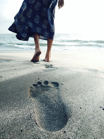 A woman walks on the beach, leaving footsteps in the sand by the ocean. HD phone wallpaper
