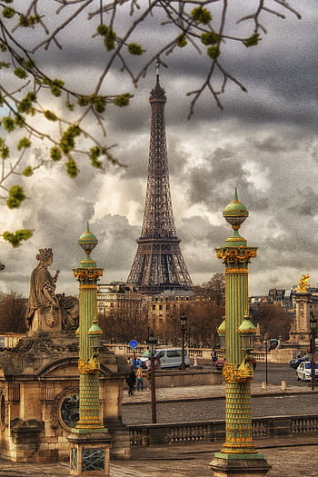 A captivating view of the Eiffel Tower framed by historic sculptures and columns in Paris under a cloudy sky. HD phone wallpaper