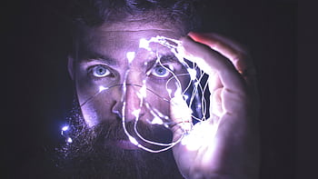 Close-up of a man with a beard holding glowing string lights, creating a mystical atmosphere. HD wallpaper