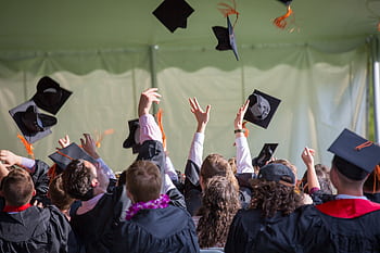 Group of graduates celebrating by tossing caps into the air during a graduation ceremony. HD wallpaper
