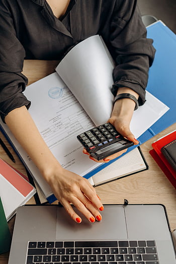 A business professional uses a calculator among documents and laptop on a desk for financial tasks. HD phone wallpaper