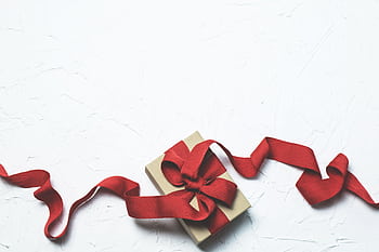 An elegant gift box with a flowing red ribbon on a textured white background, perfect for celebrations. HD wallpaper