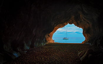 View of a sailboat from within a dark cave opening out to the bright sea. HD wallpaper