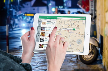 Hands using a digital map on a tablet in an urban setting at night, illustrating navigation and technology. HD wallpaper