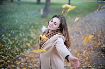 Young woman with arms outstretched, delighting in fallen leaves in a Paris park during autumn daytime. HD wallpaper