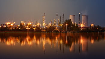 Industrial plant with reflection in water at twilight, showing smoke stacks and lights. HD wallpaper