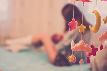A mother cradling her baby next to a dreamy cloud and star mobile in a soft-focus bedroom setting. HD wallpaper