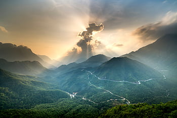 A stunning view of a sunlit mountain landscape showcasing dramatic clouds and winding roads. HD wallpaper