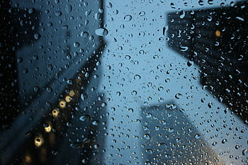 Raindrops on a window with blurred city buildings at night, capturing a moody urban scene. HD wallpaper