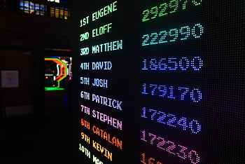 Colorful illuminated arcade scoreboard displaying high scores in a vibrant gaming ambiance. HD wallpaper