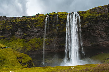 Scenic view of Seljalandsfoss waterfall in Iceland, surrounded by lush green moss and rocks. HD wallpaper