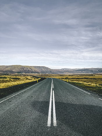 A straight road leading through the que landscapes of Iceland's countryside under a cloudy sky. HD phone wallpaper