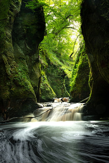 A tranquil waterfall flowing through a mossy, lush Scottish gorge, captured with long exposure. HD phone wallpaper