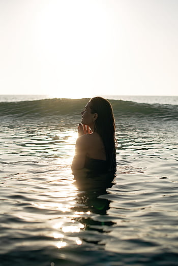 A serene scene of a young woman in the ocean at sunset, enjoying the tranquil water and peaceful ambiance. HD phone wallpaper