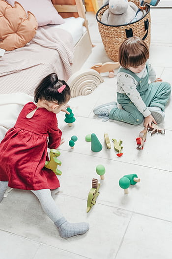 Two young children sitting on the floor enjoying playing with wooden toys. HD phone wallpaper