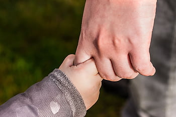 A close-up of a child and parent holding hands in a park, symbolizing love and trust. HD wallpaper