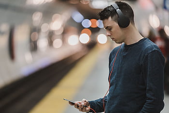 A man uses heads and a smart while waiting at a subway station. HD wallpaper