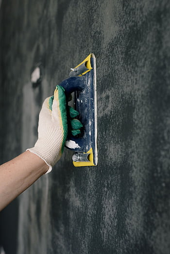 Close-up of a gloved hand using a plastering tool to smooth a wall indoors. HD phone wallpaper