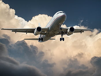 A commercial airplane flying through dramatic clouds, showcasing aviation in action. HD wallpaper