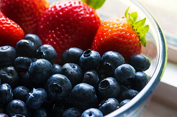 Close-up of fresh blueberries and strawberries in a glass bowl, showcasing vibrant colors and healthy appeal. HD wallpaper