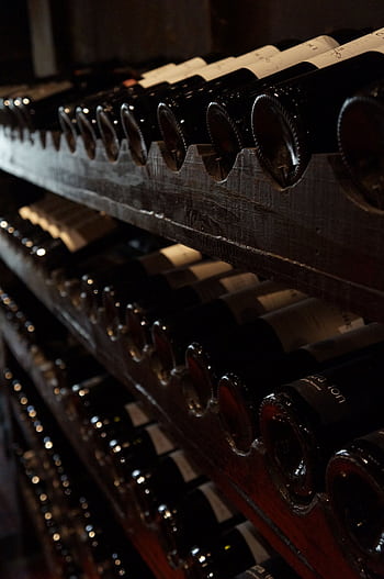 A dimly lit wine cellar showcasing rows of wine bottles on rustic wooden shelves, creating a classic and elegant atmosphere. HD phone wallpaper