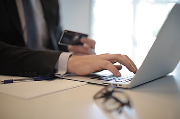 Man in suit using laptop and credit card for online transaction at work. HD wallpaper