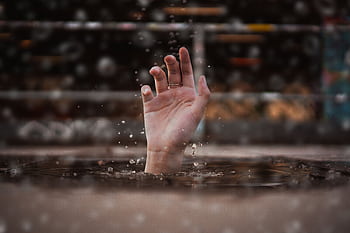 A single hand emerges from water, symbolizing a cry for help amidst a rainy setting. HD wallpaper