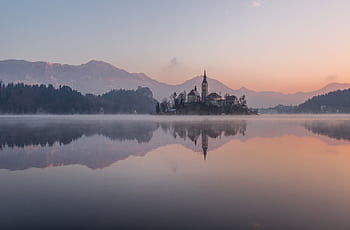 Tranquil morning view of Lake Bled with misty reflections and church silhouette. HD wallpaper