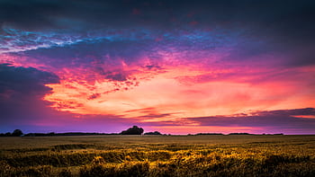 A stunning view of a colorful sunset over a serene rural landscape with fields and dramatic clouds. HD wallpaper