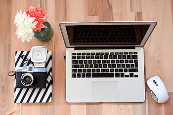 A modern home office setup featuring a laptop, vintage camera, and flowers, perfect for lancers. HD wallpaper