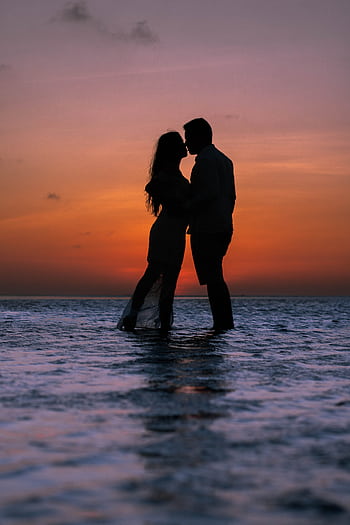 Silhouette of a couple kissing at the beach during a vibrant sunset, creating a romantic ambiance. HD phone wallpaper