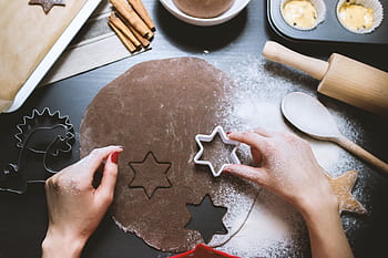 Hands cutting star-shaped cookies from chocolate dough, surrounded by baking tools. HD wallpaper